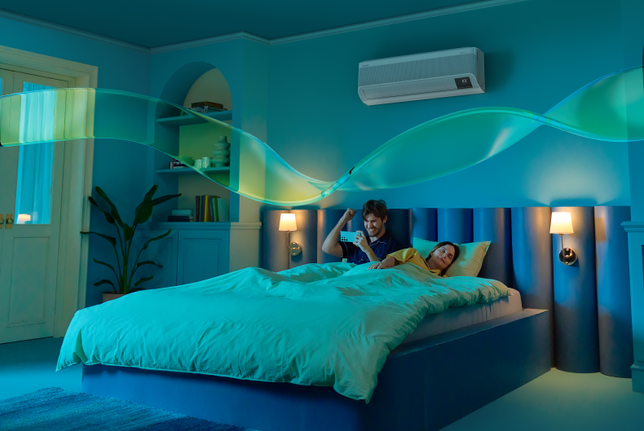 A man uses his phone in bed while a woman sleeps. WindFree mode is activated, with 23dB(A) low noise operation through 23,000 micro air holes.